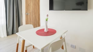 A modern room with a white table, a red placemat, a white chair, a wooden door, and a mounted TV. - Hache Palermo by IPPA (Buenos Aires)
