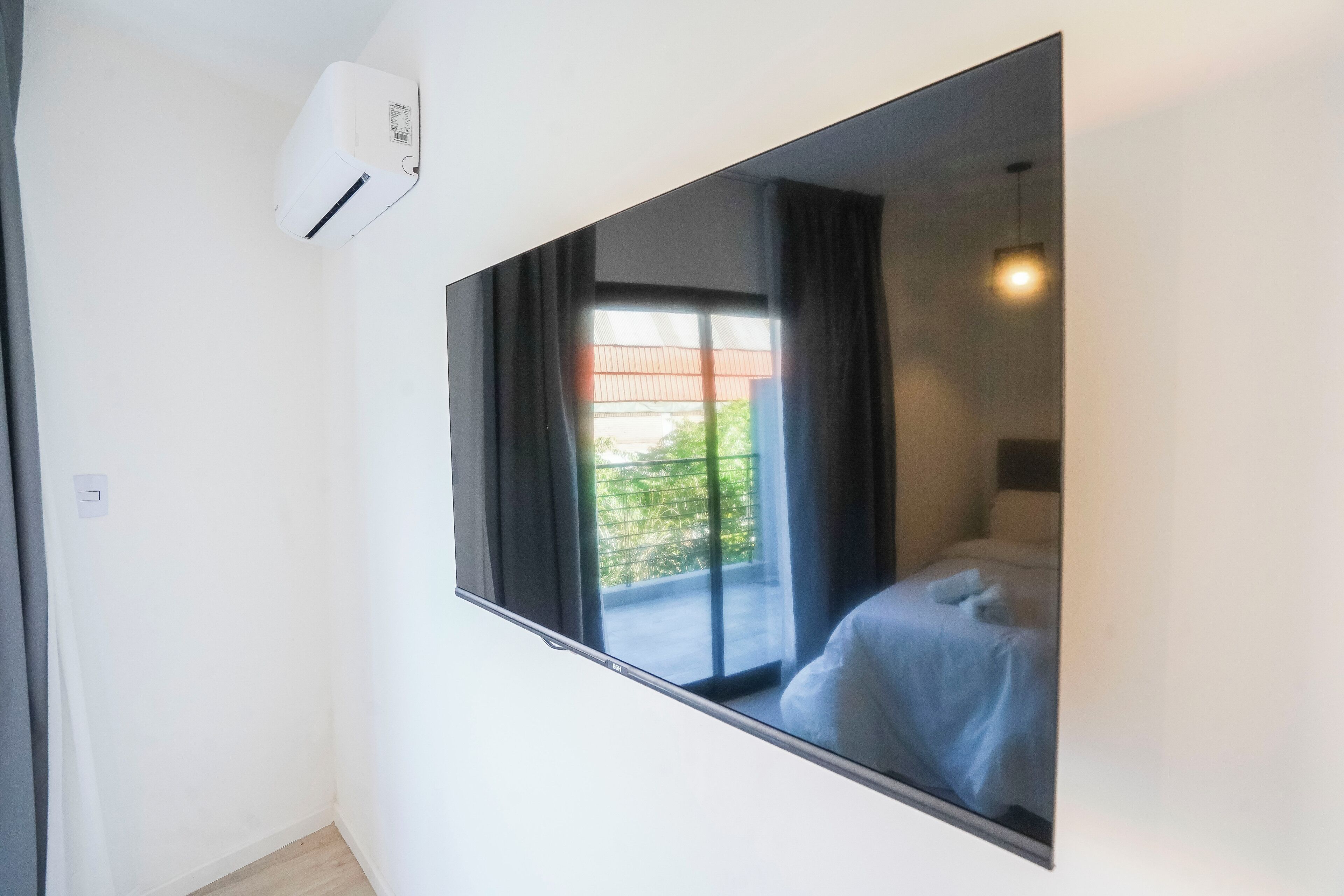 A room with a large window, a bed, a bedside table, and a wall-mounted air conditioner.