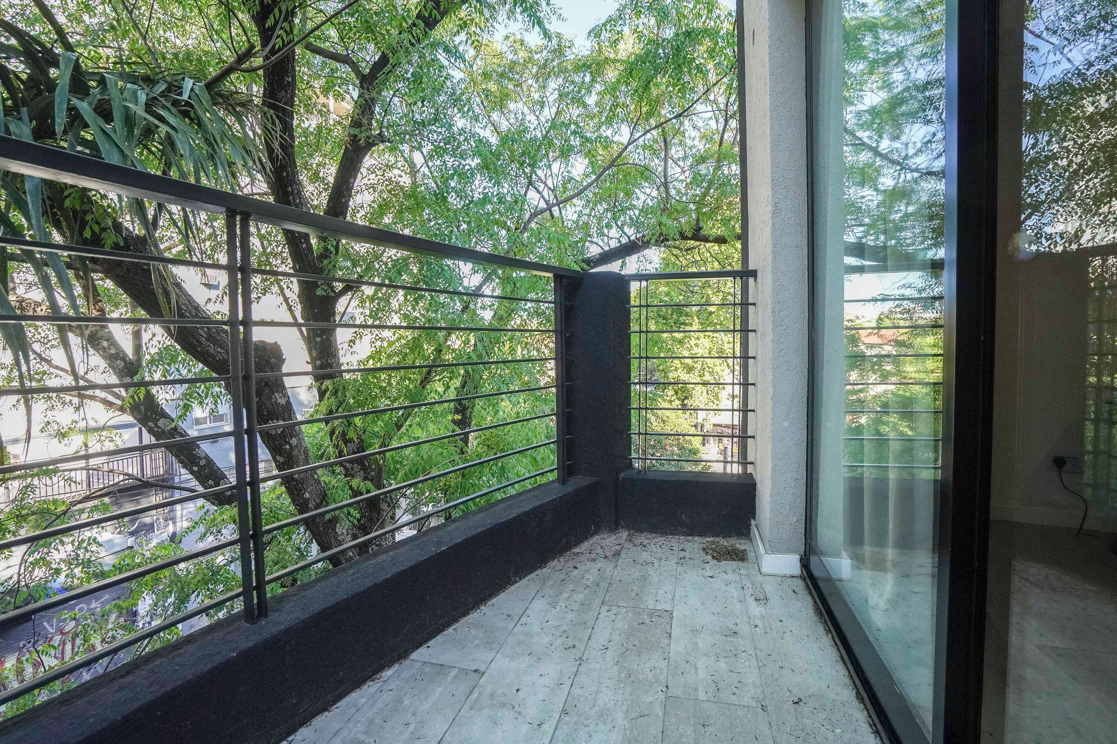 Ein Balkon mit Metallgeländer, Fliesenboden und Blick auf Bäume und Gebäude.