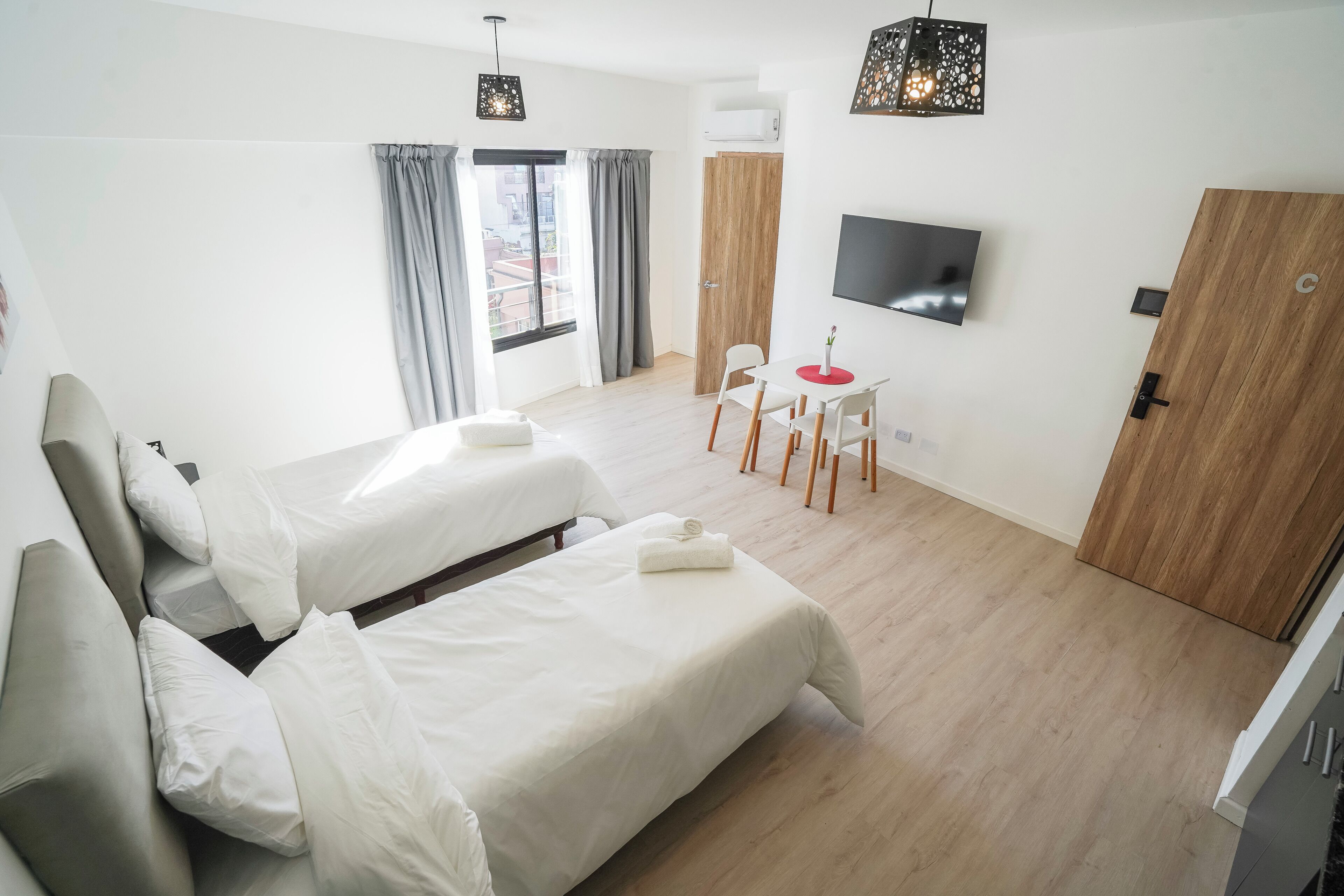 Ein Hotelzimmer mit zwei Betten, einem Fernseher, einem Schreibtisch mit Stühlen und einer Holztür.