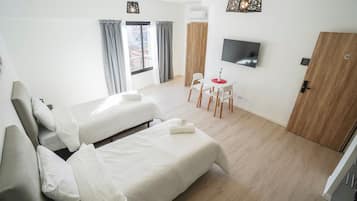 Ein Hotelzimmer mit zwei Betten, einem Fernseher, einem Schreibtisch mit Stühlen und einer Holztür.