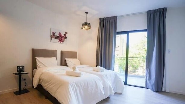 A bedroom with a bed, a bedside table, a hanging light fixture, and a window with curtains. - Hache Palermo by IPPA (Buenos Aires)