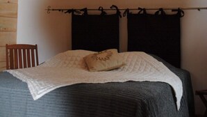 Ein Schlafzimmer mit einem Bett, zwei Wandleuchten, einem Holzstuhl und einem Vorhang an der Kopfteil.