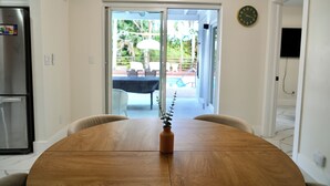 A dining area with a wooden table, a vase with a plant, and a view of an outdoor patio with chairs and umbrellas. - Hollywood 1811 (Hollywood)