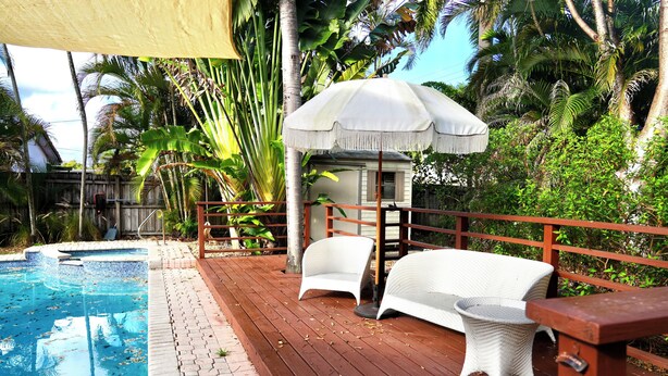 A poolside area with a wooden deck, white wicker furniture, and a canopy. - Hollywood 1811 (Hollywood)