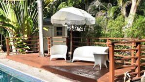 A wooden deck with a pool, white chairs, a small table, and an umbrella. - Hollywood 1811 (Hollywood)
