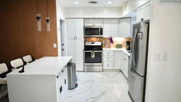 A modern kitchen with white cabinets, a stainless steel refrigerator, a microwave, and a stove.