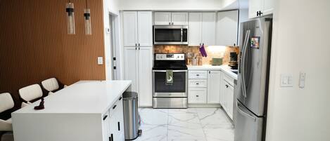 A modern kitchen with white cabinets, a stainless steel refrigerator, a microwave, and a stove.