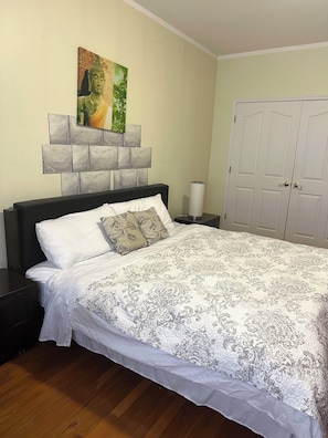 A bedroom with a bed, a headboard with a Buddha painting, a white door, and a nightstand with a lamp.