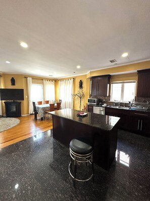 A modern kitchen with a central island, dark countertops, and a dining area with a table and chairs.