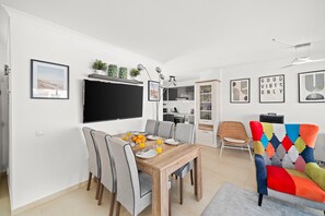 Un salon moderne comprenant un coin repas, un téléviseur à écran plat et un fauteuil coloré.