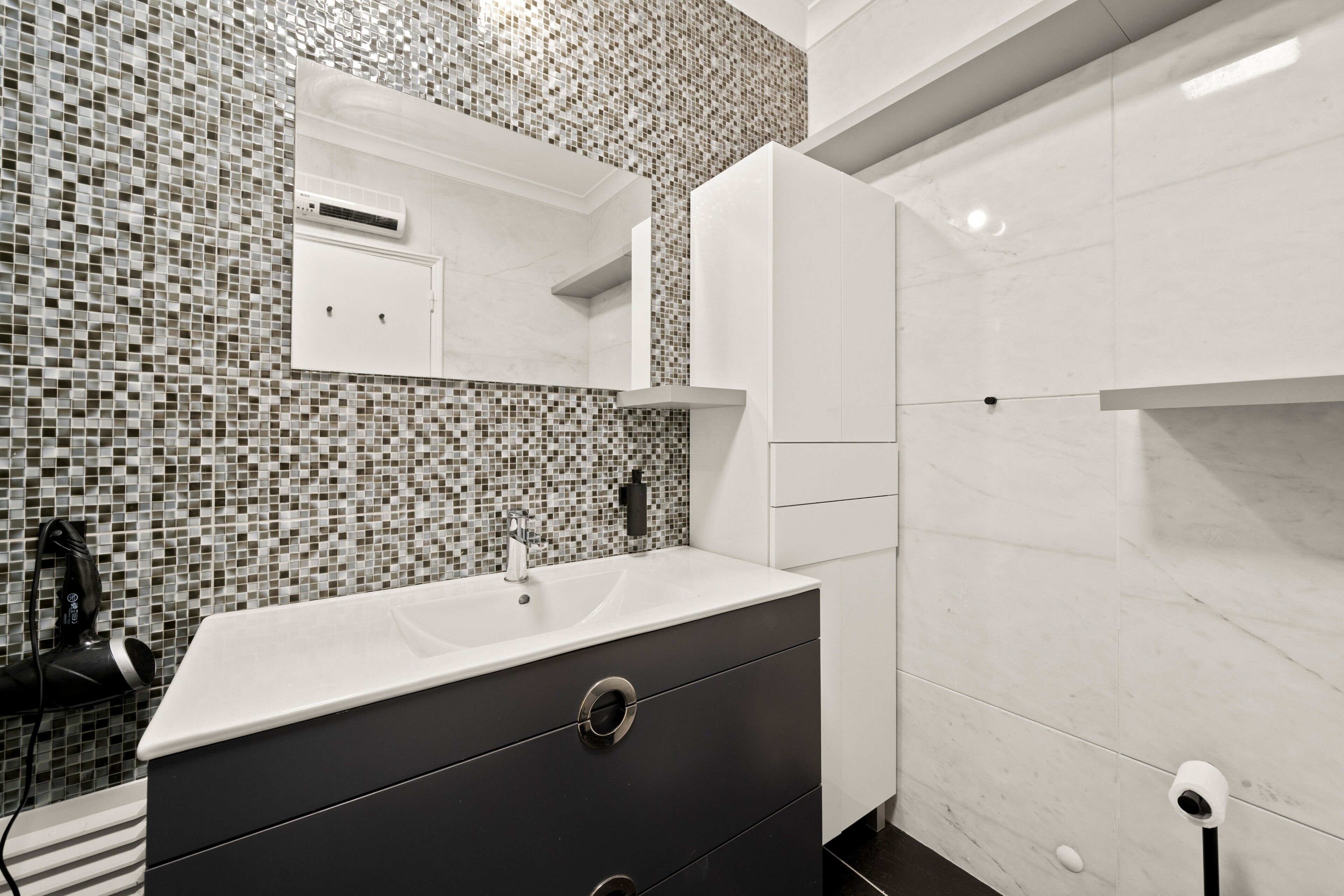 A bathroom with a tiled mosaic backsplash, a white sink, a mirror, and a black cabinet.