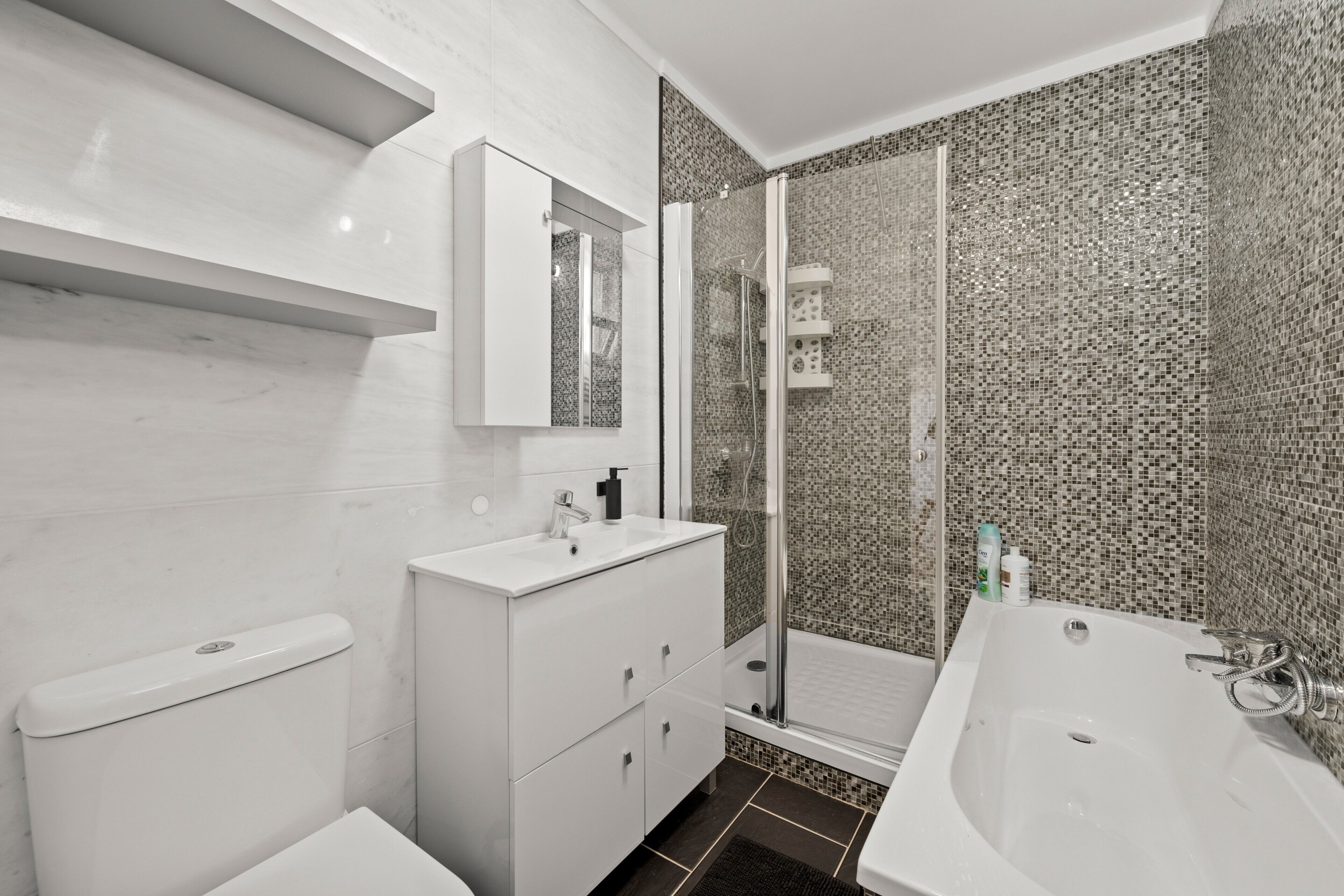 A modern bathroom with a toilet, a vanity with a mirror, a shower area, and a bathtub.