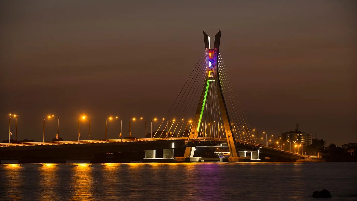 A cable-stayed bridge at night with illuminated cables and lights reflecting on the water.