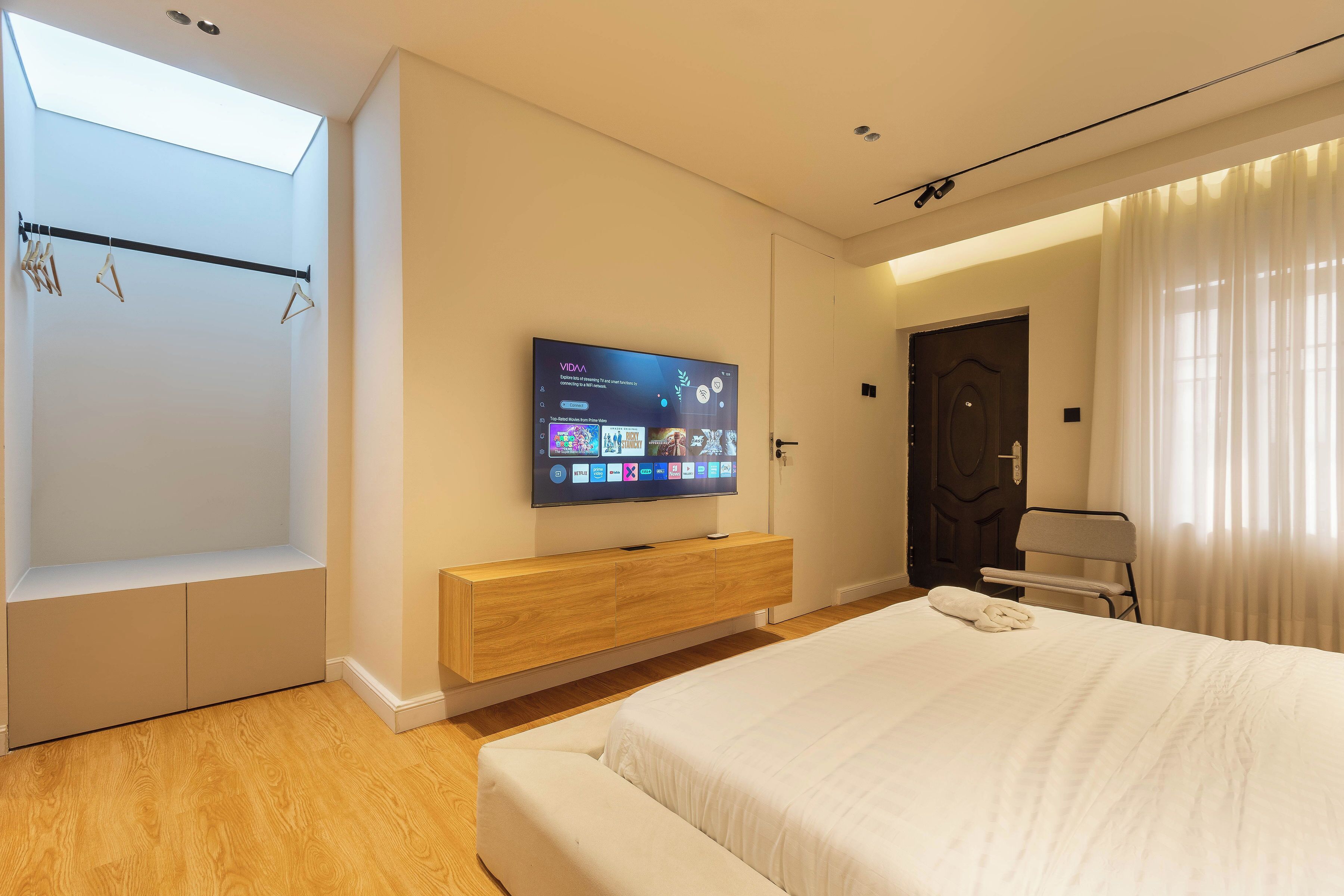 A modern hotel room with a bed, a TV mounted on a wooden console, a wardrobe, and a skylight.