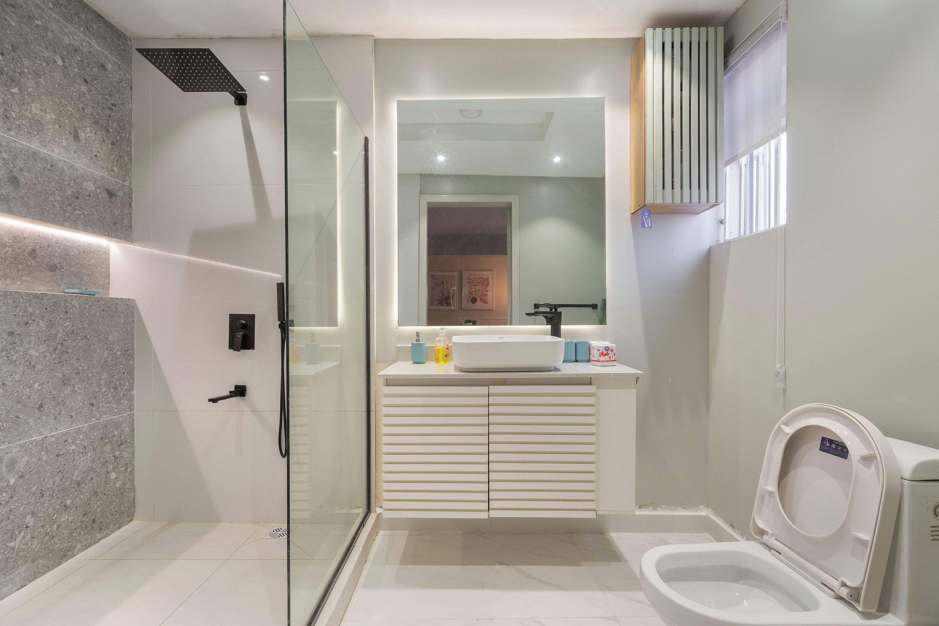 Een moderne badkamer met een douchecabine van glas, een witte wastafel met spiegel erboven en een toilet met deksel.