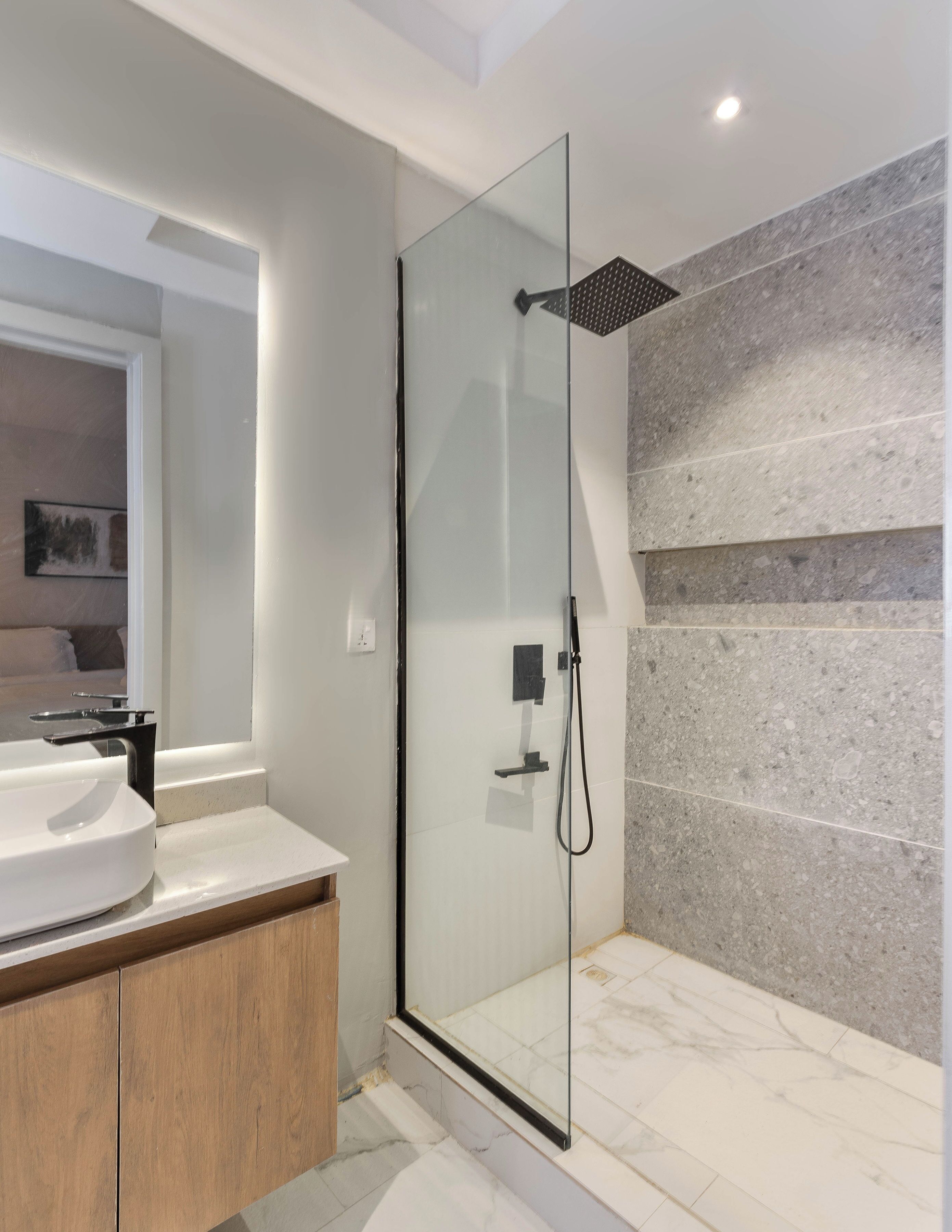 Un baño moderno con ducha envuelta en vidrio, un lavabo blanco y suelo de mármol.