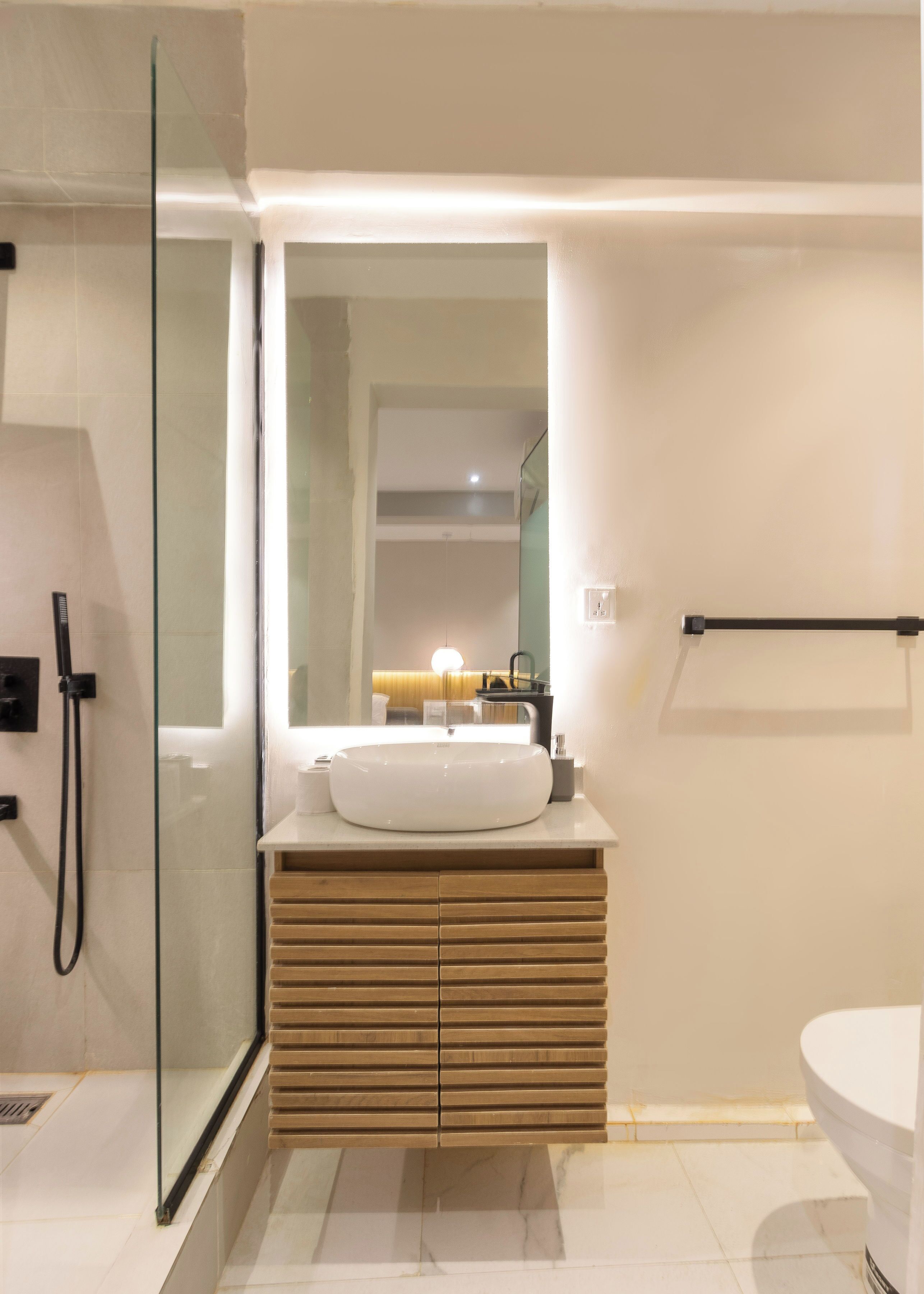 Une salle de bain moderne avec une douche à parois de verre, un lavabo blanc avec un meuble-vasque en bois et un grand miroir.