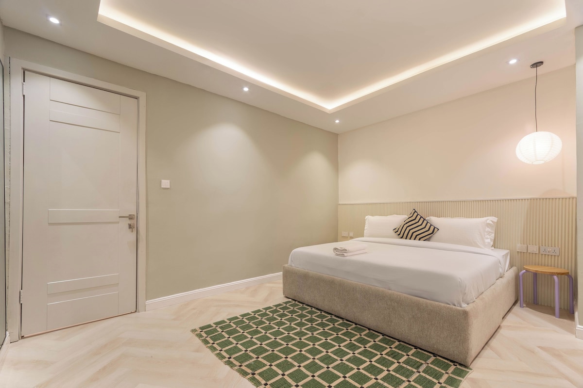 A modern bedroom with a bed, bedside table, and a hanging light fixture.