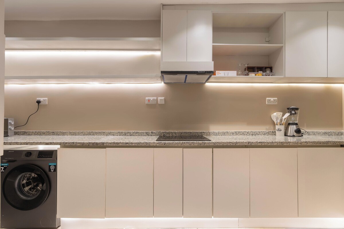 A modern kitchen with a built-in washing machine, a granite countertop, and white cabinetry.