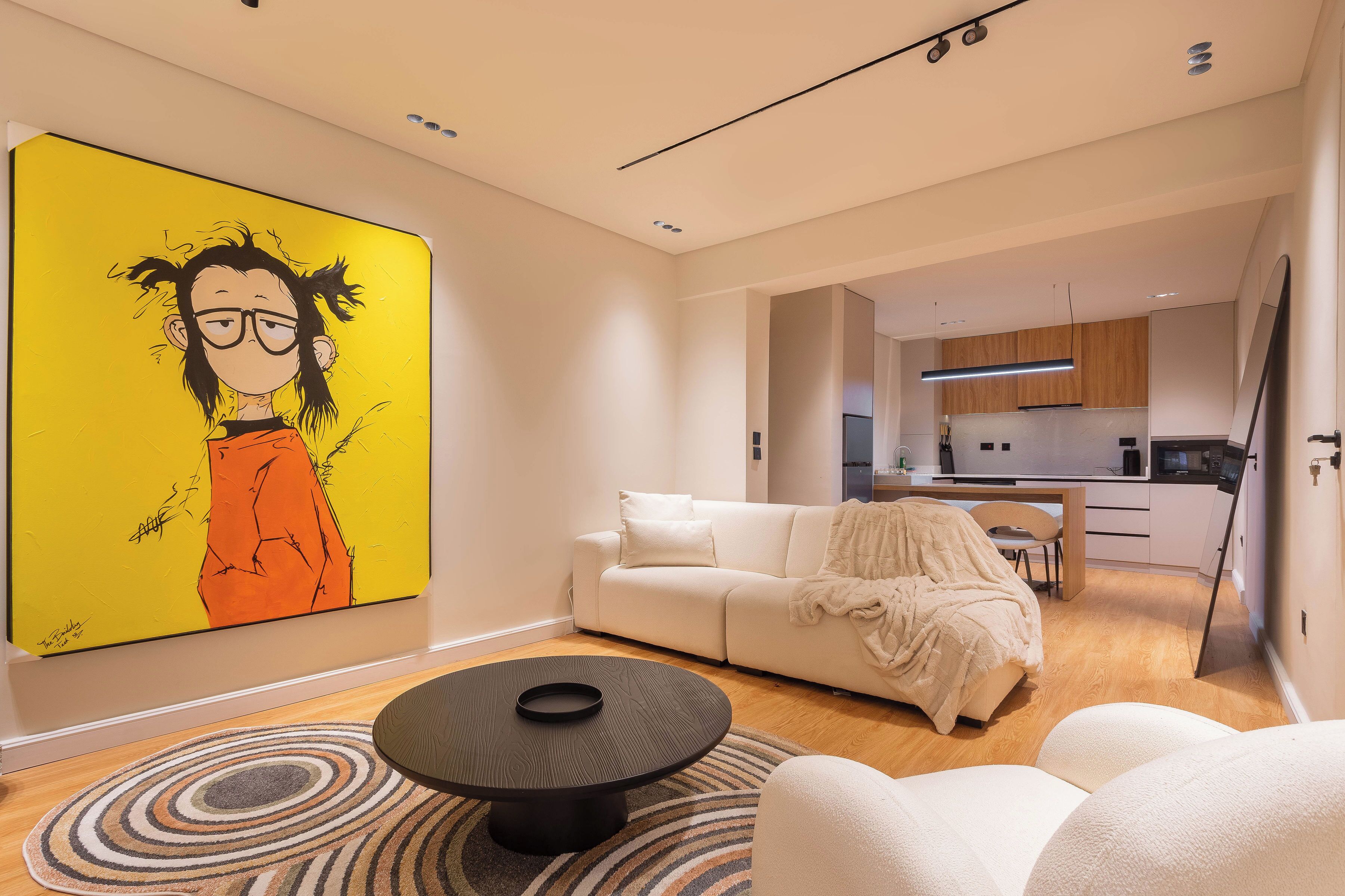 Een moderne woonkamer met een groot kunstwerk, een witte bank, een salontafel en een keuken op de achtergrond.