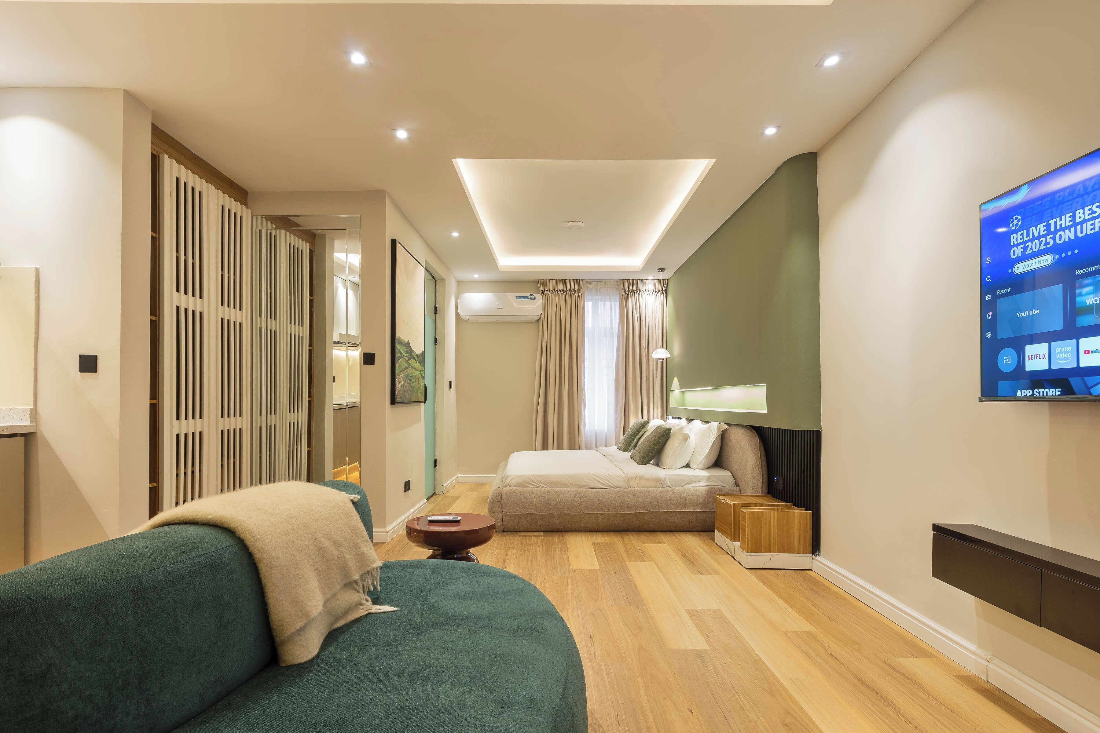 Habitación de hotel moderna con sofá, cama, televisión y suelo de madera.