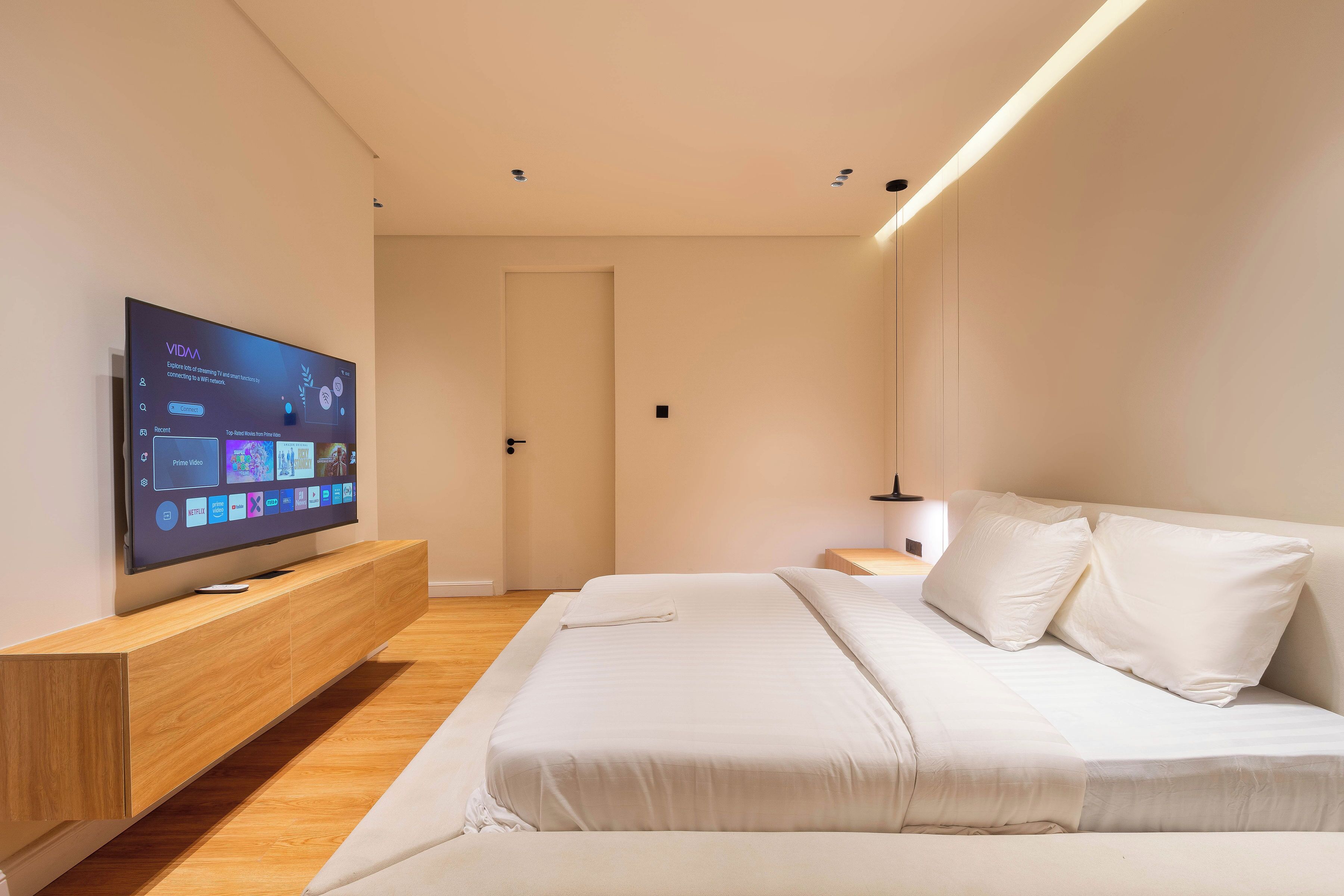 A modern bedroom with a flat-screen TV, a wooden bedside table, a bed with white bedding, and a nightstand.