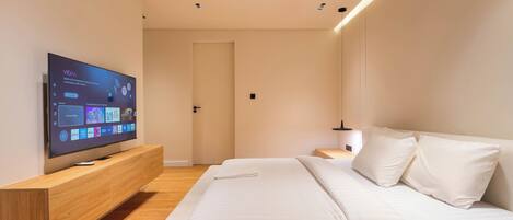 A modern bedroom with a flat-screen TV, a wooden bedside table, a bed with white bedding, and a nightstand.