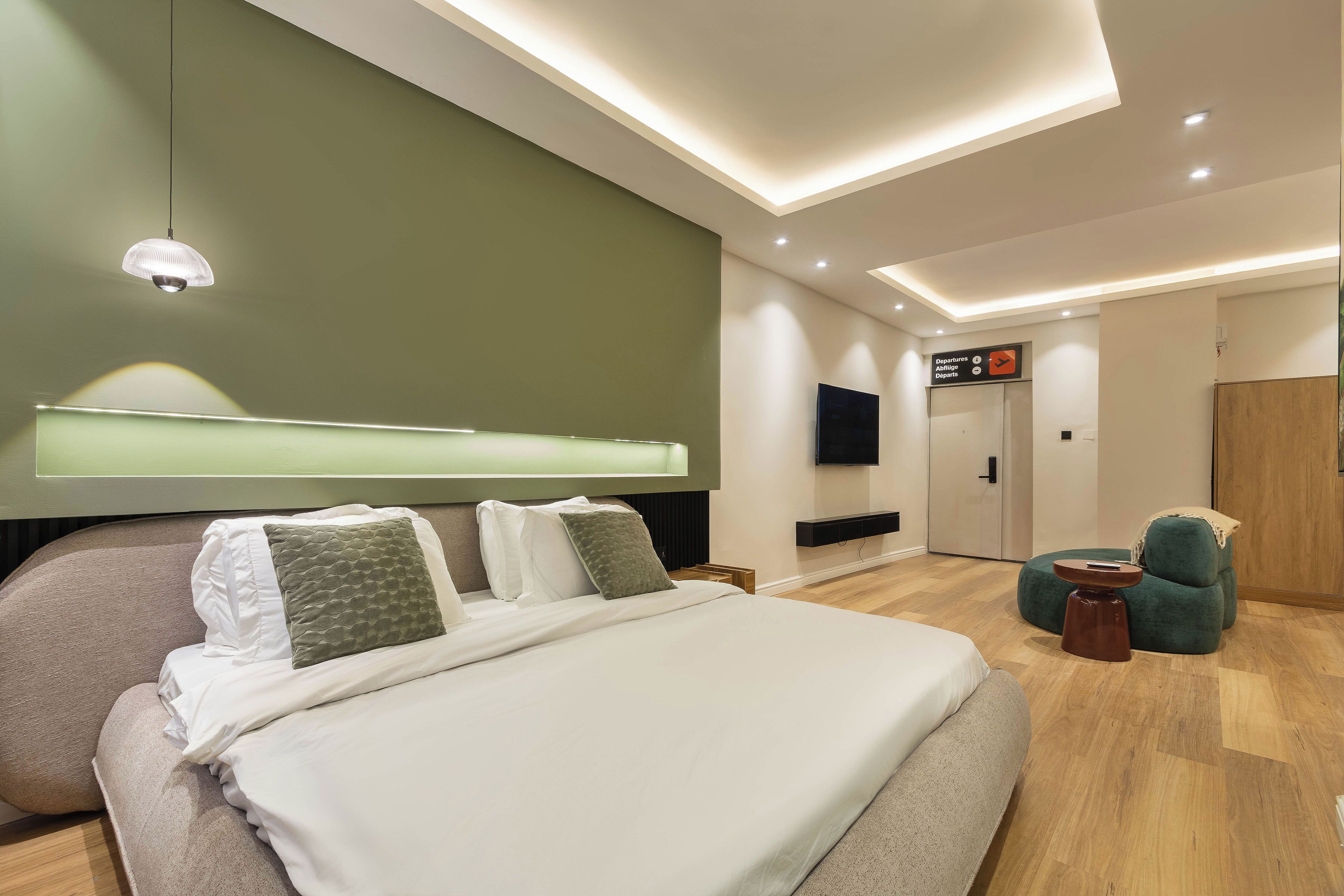 Quarto de hotel moderno com uma cama grande, televisão, escrivaninha e área de estar.