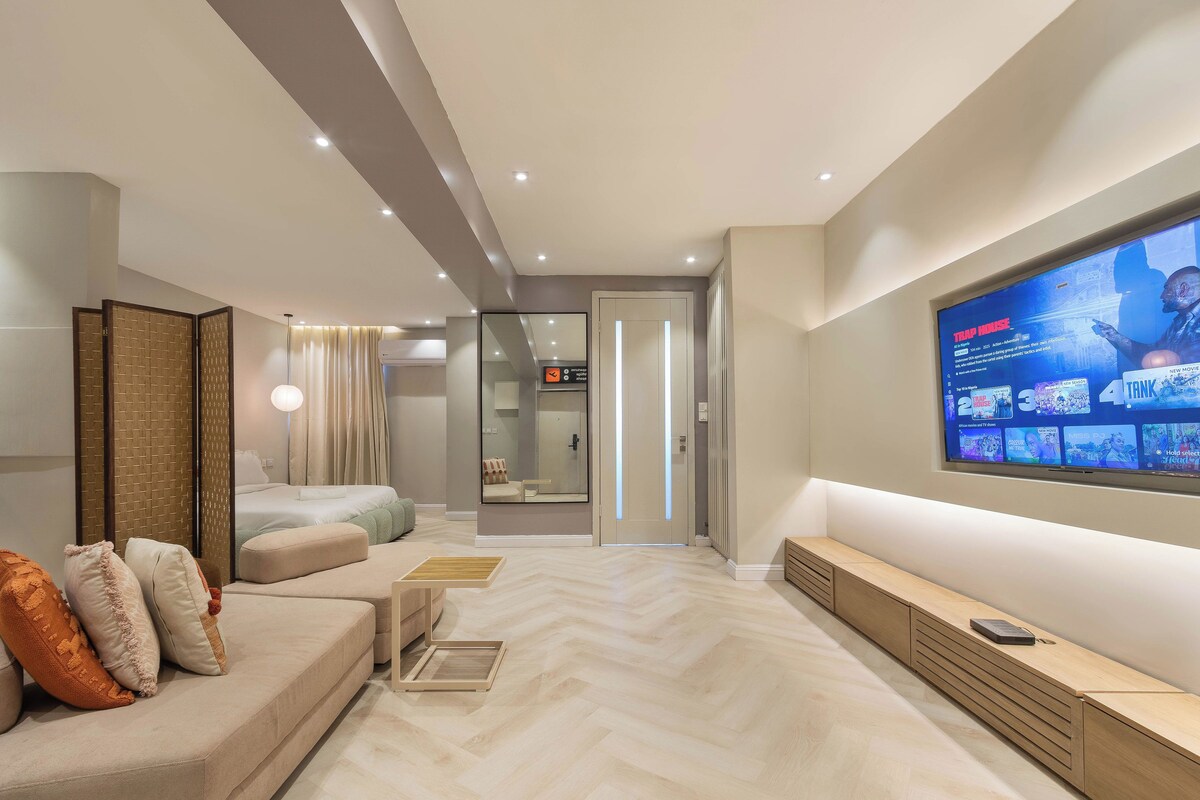 A modern living room with a large TV, a sofa, a wooden bench, and a herringbone-patterned floor.