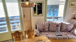 A dining area with a wooden table and chairs, a hanging light fixture, and a sofa with patterned cushions. - 6-PERSON APARTMENT PRALOGNAN LA VANOISE (Pralognan-la-Vanoise)