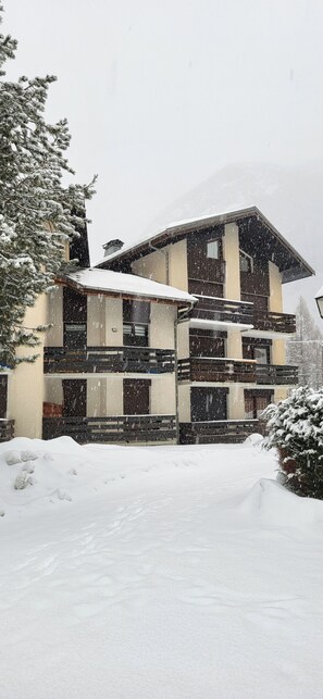 Ein mehrgeschossiges Gebäude mit verschneitem Dach und umliegender Schnee.