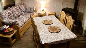 A cozy living room with a sofa, a dining table with chairs, a hanging light fixture, and a fireplace. - 6-PERSON APARTMENT PRALOGNAN LA VANOISE (Pralognan-la-Vanoise)