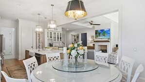 A modern dining area with a glass table, white chairs, and a chandelier. - Stop-n-Beach Inn-Coastal Luxury in the Heart of St. Simons Island (Saint Simons Island)