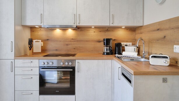 A modern kitchen with light wood cabinetry, stainless steel appliances, and a built-in oven. - Apartment 'Ferienwohnungen Meerblick -' with Private Terrace, Garden View, and Wi-Fi (Bastorf)