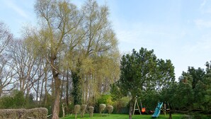 A grassy area with a playground, including a slide and swings, surrounded by trees and a hedge. - Apartment 'Ferienwohnungen Meerblick -' with Private Terrace, Garden View, and Wi-Fi (Bastorf)