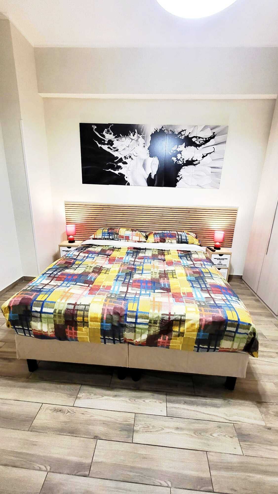 A bedroom with a bed, a headboard, a wall art piece, and a wooden floor.