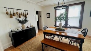 Un espace repas comprenant une table en bois, des chaises, un banc, une console noire et des luminaires fixés au mur.