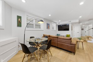 Una sala de estar moderna con una mesa de comedor de vidrio, sillas negras, un sofá marrón y un televisor.