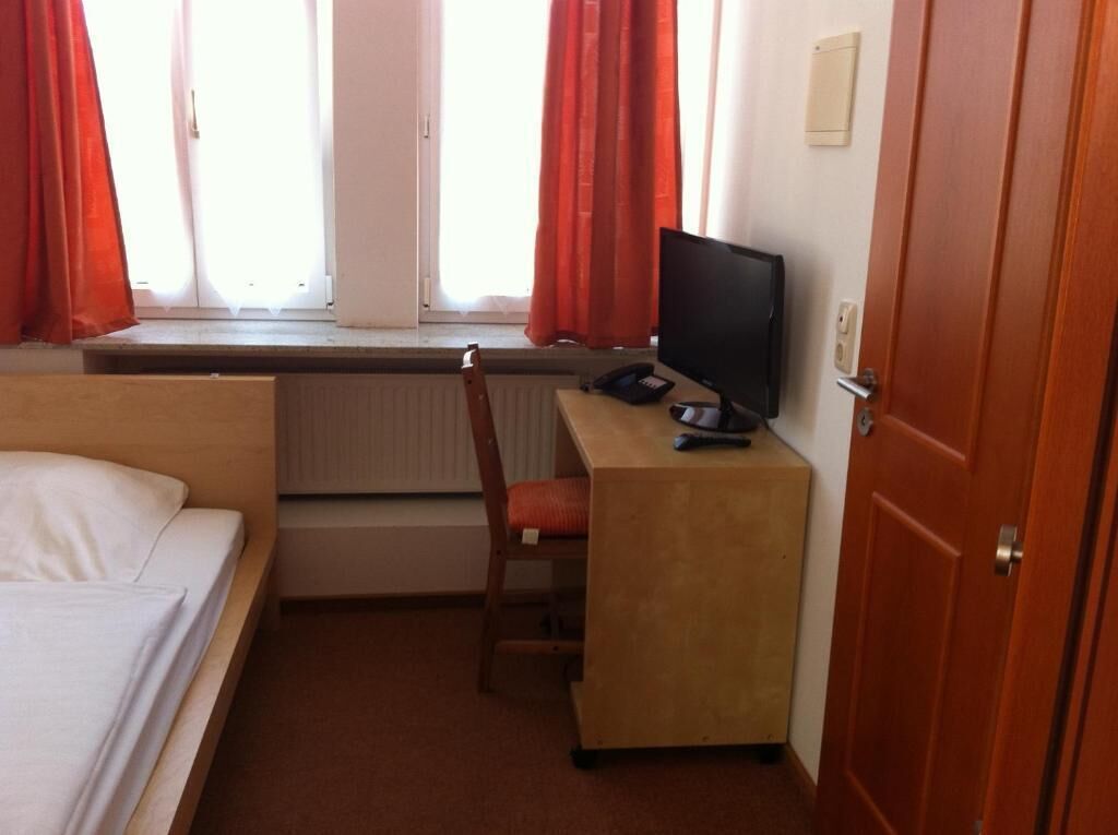 Une chambre d’hôtel avec un lit, un bureau avec un ordinateur, une chaise et une fenêtre avec des rideaux.