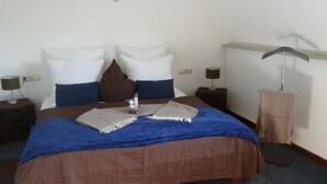 A neatly made bed with a blue and brown bedspread, two white pillows, a brown accent pillow, and a small bedside table with a lamp. - Hotel Zum Bügeleisen (Duisburg)