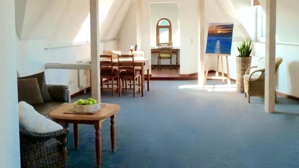 A spacious attic room with a dining area, a painting on the wall, and a view through a window. - Hotel Zum Bügeleisen (Duisburg)