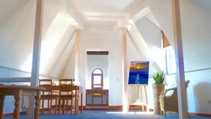 A room with a high ceiling, wooden beams, a dining table with chairs, a painting on the wall, and a potted plant. - Hotel Zum Bügeleisen (Duisburg)