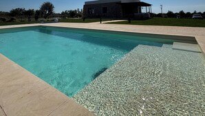 En klar, blå swimmingpool med en sol i skyerne og en bygning i baggrunden.