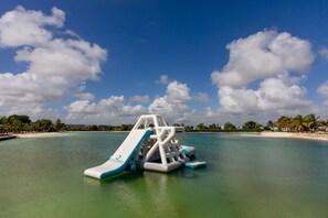 A water park with a large slide and a play structure in the middle of a turquoise sea, surrounded by palm trees and a clear sky. - 2 bedrooms first floor, pool and gym (Punta Cana)