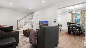 Uma sala de estar moderna com sofá, apoio para os pés e área de jantar com cadeiras e mesa.