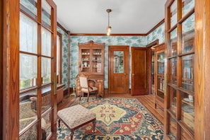 A room with large wooden bookshelves, a patterned rug, and a chair. - The Painted Petal: A Historic 5 Bedroom Mini Estate Perfect for Groups (Breinigsville)