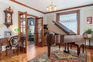 A grand piano, a wooden chair, a green bowl, and a large mirror in a room with wooden floors and a patterned rug. - The Painted Petal: A Historic 5 Bedroom Mini Estate Perfect for Groups (Breinigsville)