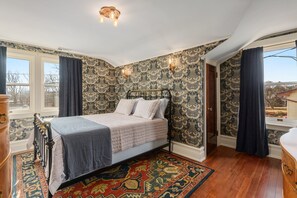 Un dormitorio con cama, papel tapiz estampado, una ventana con cortinas y suelo de madera.