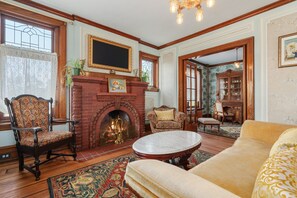 A traditional living room with a fireplace, a sofa, a patterned armchair, and a dining area. - The Painted Petal: A Historic 5 Bedroom Mini Estate Perfect for Groups (Breinigsville)